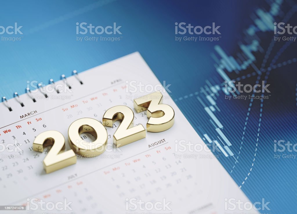 Gold colored 2023 sitting over a white calendar on blue financial graph. Horizontal composition with selective focus and copy space. Investment, stock market data and financial planning concept.